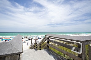 A wooden boardwalk leading to a beach with umbrellas and people.