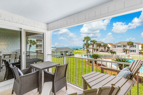 A balcony with wicker furniture, a view of the ocean, and a pool area.