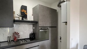 A modern kitchen with grey cabinets, a built-in oven, and a gas stove. There is a dining area with a white table and two chairs. - Modern apartment on the Adriatic coast. Only 2 minutes from the beach (Lido Adriano)