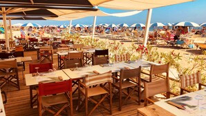 An outdoor dining area with wooden tables and chairs, covered by large umbrellas. - Modern apartment on the Adriatic coast. Only 2 minutes from the beach (Lido Adriano)