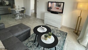 A modern living room with a sofa, two coffee tables, a TV, and a dining area. - Modern apartment on the Adriatic coast. Only 2 minutes from the beach (Lido Adriano)