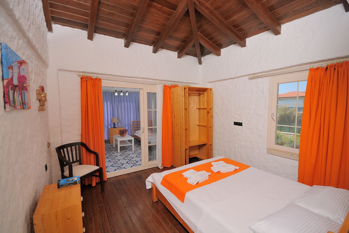 A bedroom with a wooden bed, orange curtains, a wooden chair, and a small table.