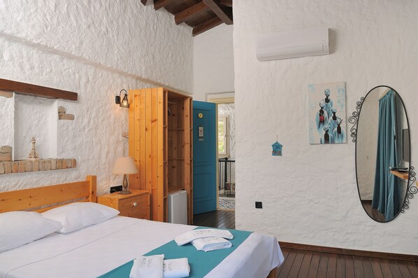 Une chambre à coucher avec un lit, une tête de lit en bois, une table de chevet, une lampe, une porte bleue, un miroir et un climatiseur fixé au mur.