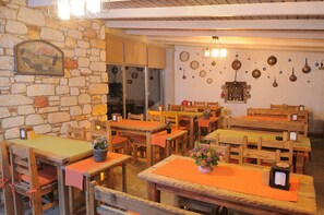 Um restaurante com mesas e cadeiras de madeira, paredes de pedra e diversos utensílios de cozinha pendurados na parede.