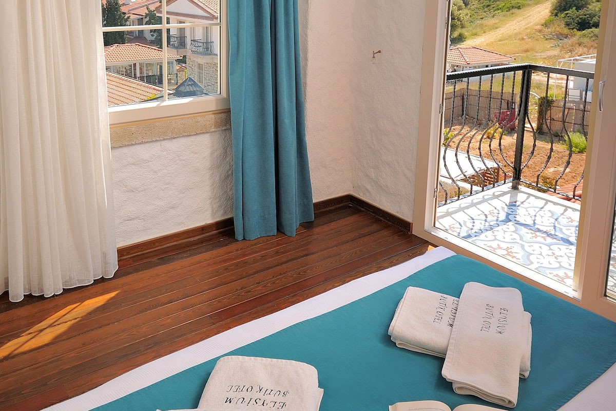 A room with a large window, a balcony, and a yoga mat with towels.