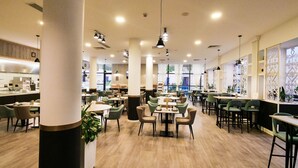 Un restaurant spacieux doté de plusieurs espaces de restauration, notamment des tables rondes et des banquettes, ainsi qu’une grande fenêtre offrant une vue sur l’extérieur.