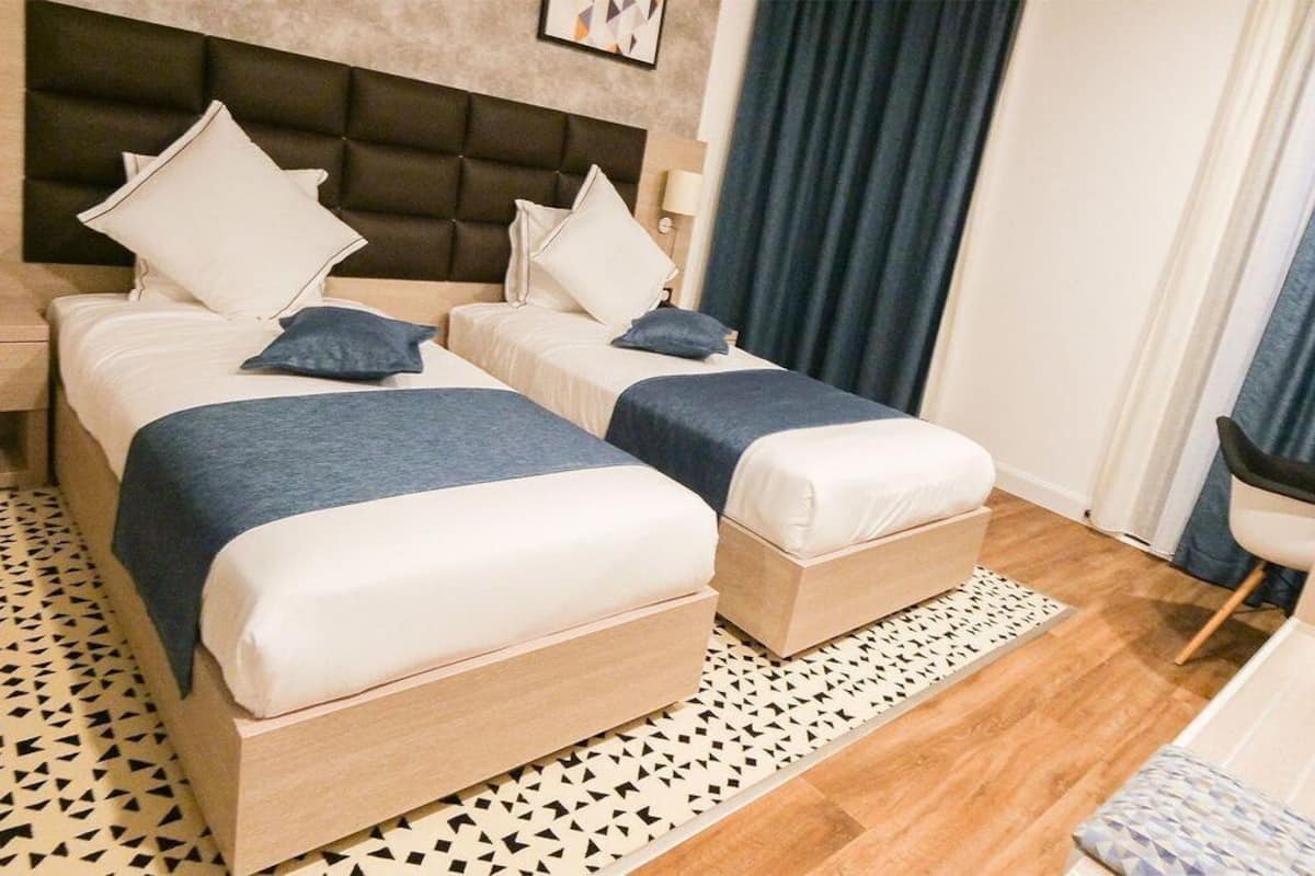 A hotel room with two beds, a nightstand, a desk, and a chair.