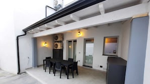 Une terrasse avec une table et des chaises, un petit barbecue et un ventilateur.