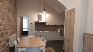 Une cuisine compacte avec une table et des chaises en bois, un mur en pierre et une vue sur une autre pièce.