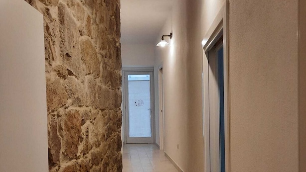 Un couloir avec un mur en pierre, une porte et un escalier menant à une pièce.