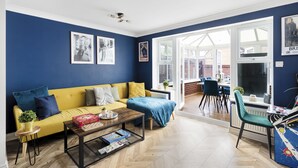 Ein Wohnzimmer mit gelber Couch, einem Couchtisch und einem Essbereich mit Stühlen und einem Tisch.