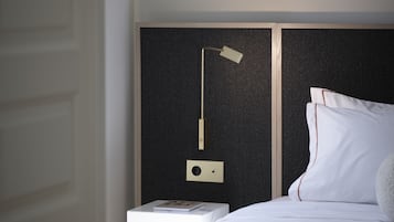 Un lit bien fait, avec du linge de lit blanc, une table de chevet sur laquelle repose un livre et une lampe moderne.