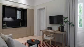 A modern living room with a sofa, a dining table, a TV, and a kitchen area with cabinets and a window.