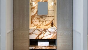 A modern bathroom with a marble vanity, wooden cabinetry, and a wall-mounted mirror. - Kinglin Luxury Living (Athens)