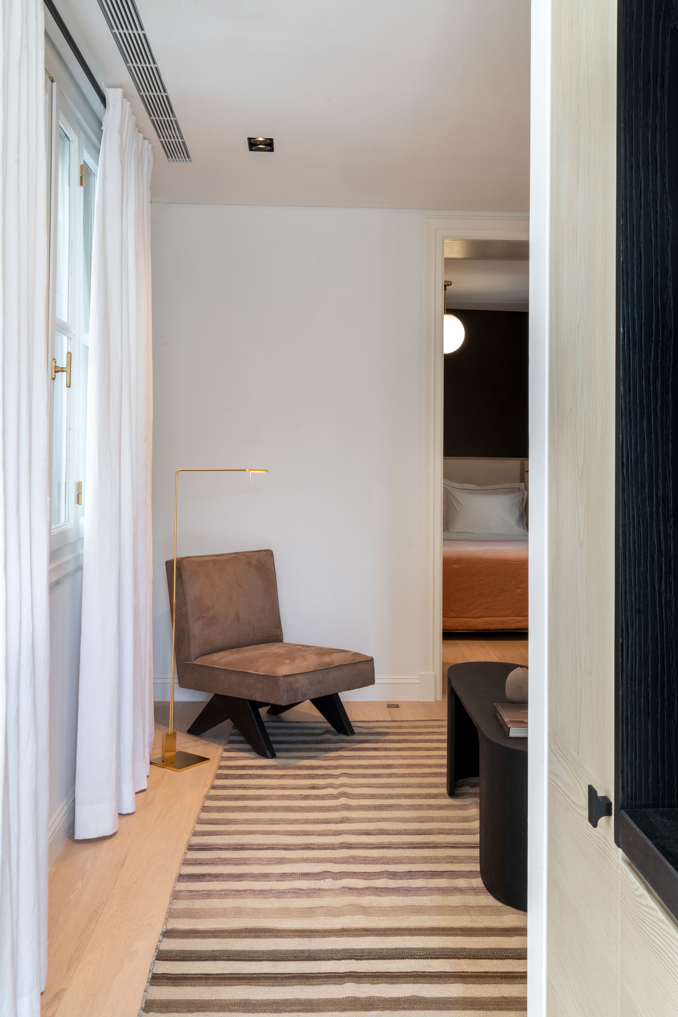 A modern bedroom with a bed, a chair, a floor lamp, and a striped rug.