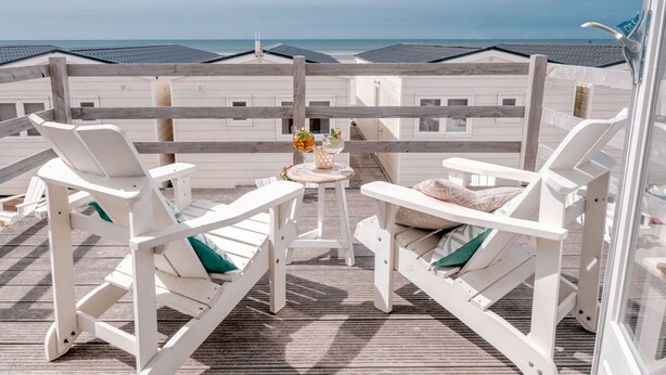 Un balcon avec des chaises longues blanches et une petite table sur laquelle se trouvent une boisson et des fruits.
