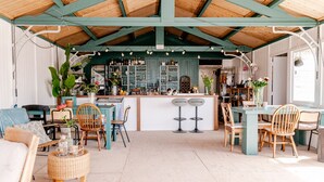 Un café chaleureux et bien éclairé, avec un plafond en bois, un coin bar doté de tabourets et un espace repas meublé de mobilier en osier.