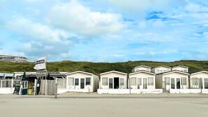Une rangée de maisons mobiles blanches, situées en bord de plage, avec un bar de plage et un snack-bar en premier plan.