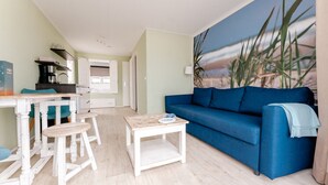 Un salon avec un canapé bleu, une table basse et un coin cuisine comprenant un comptoir et des chaises.