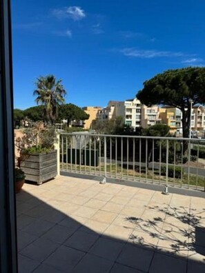 A balcony with a metal railing, a potted plant, and a view of residential buildings. - T2 apartment with large terrace (Gruissan)