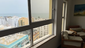A room with a large window overlooking a cityscape, a bed, and a chair. - Armação Pêra magnificent sea view 100m from the beach (Armação de Pêra)