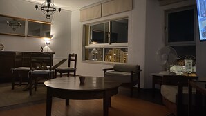 A living room with a round table, two chairs, a sofa, a TV, a fan, and a window with a view of buildings. - Armação Pêra magnificent sea view 100m from the beach (Armação de Pêra)