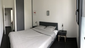 A hotel room with a large bed, bedside tables, a nightstand, a wall-mounted light, and a door leading to another room.