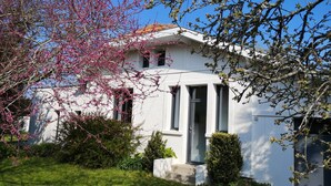 A white house with a red-tiled roof, a small front yard, and a tree with pink blossoms.