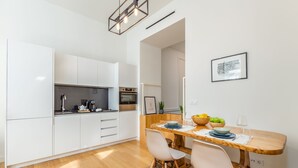 A modern kitchen with white cabinets, a wooden dining table, and a framed picture on the wall.