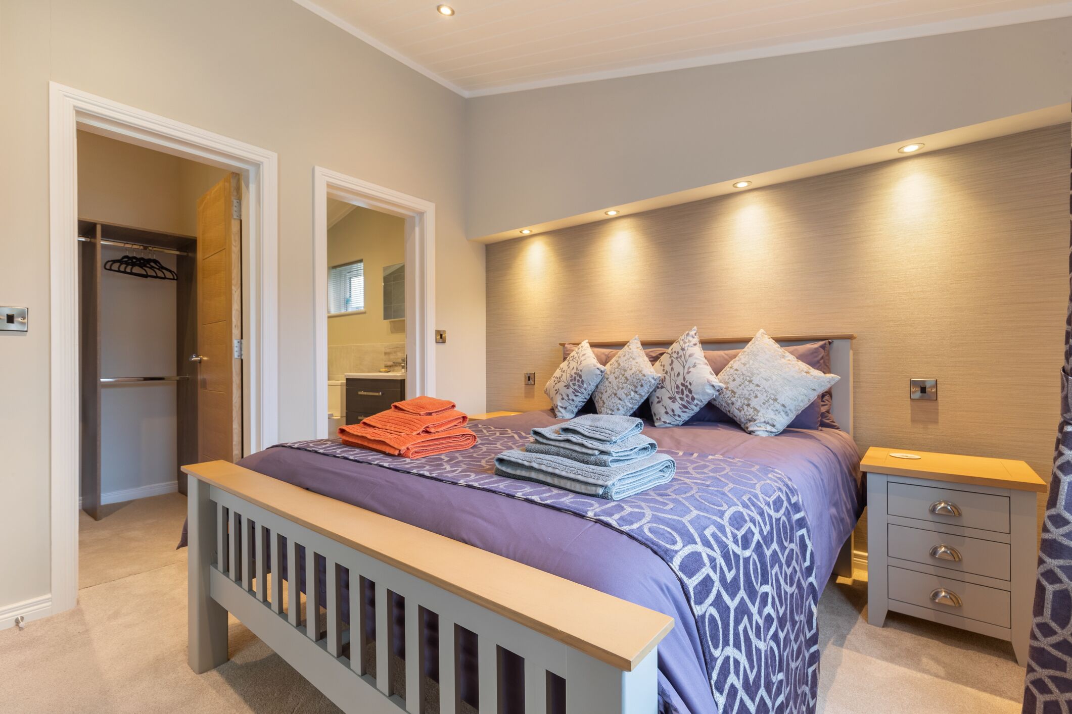 Camera da letto con un letto, un comodino, una testiera in legno, un armadio e un bagno visibile attraverso una porta aperta.