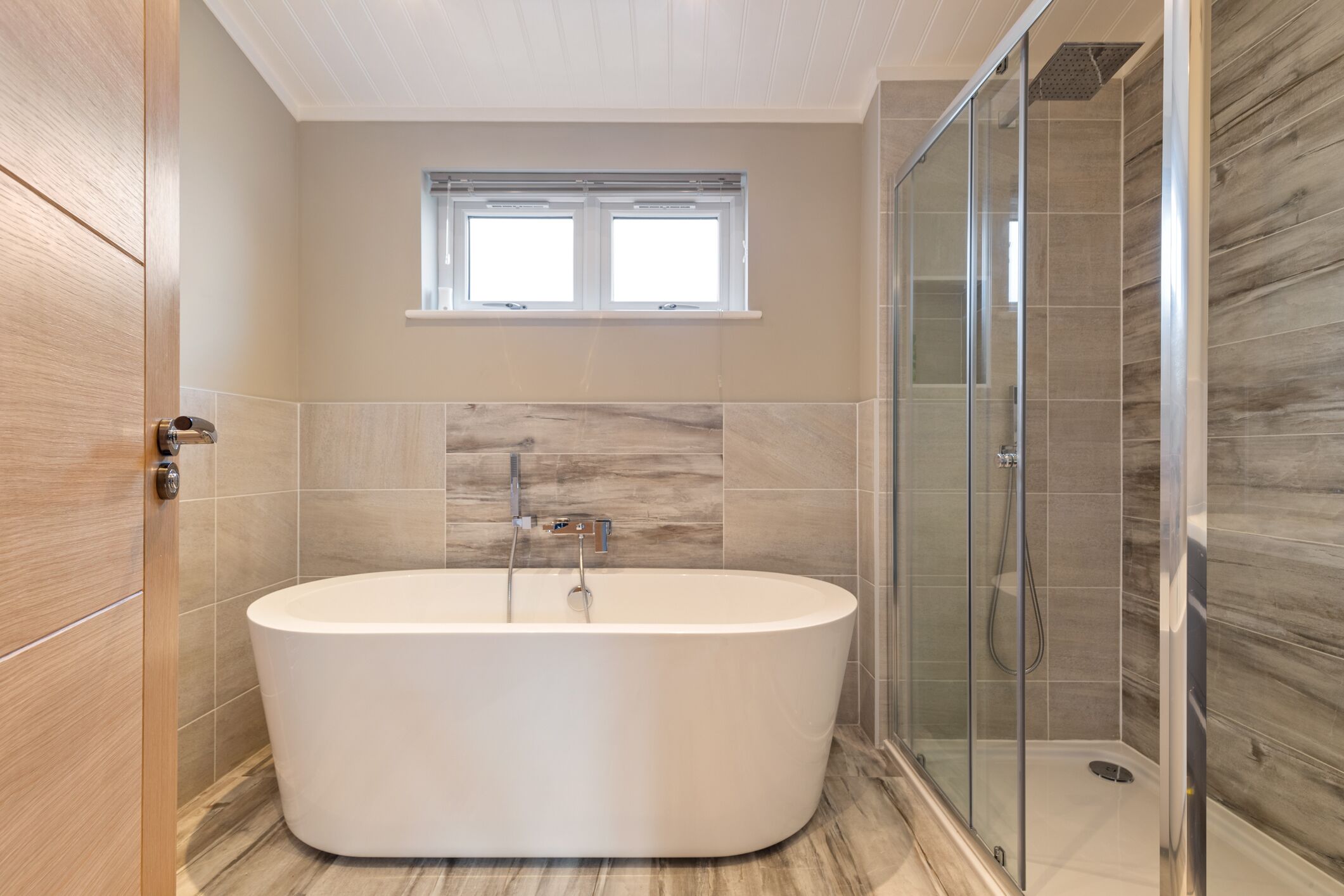 A modern bathroom with a freestanding bathtub, a glass-enclosed shower, and a window above the tub.