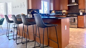 Une cuisine moderne avec des meubles en bois, un îlot central doté de tabourets, un four encastré et une machine à café.