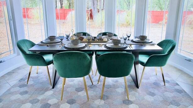Un coin repas avec une table dressée pour six personnes, entouré de chaises vertes aux pieds dorés, et un sol orné d’un motif hexagonal.