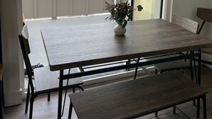 A dining area with a table and benches, a vase with flowers, and a view of a parking lot and trees through a sliding glass door. - Oceanside beach retreat 3 min walk to beach Rooftop views (Oceanside)