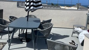 A rooftop terrace with a table and chairs, a striped umbrella, and a view of palm trees and the ocean. - Oceanside beach retreat 3 min walk to beach Rooftop views (Oceanside)