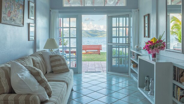 Una habitación con sofá, lámpara, estantería y vistas al mar a través de puertas abiertas.
