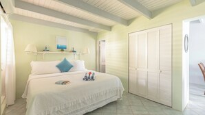 Un dormitorio con cama, almohadas, mesita de noche con lámpara, ventana y puerta.