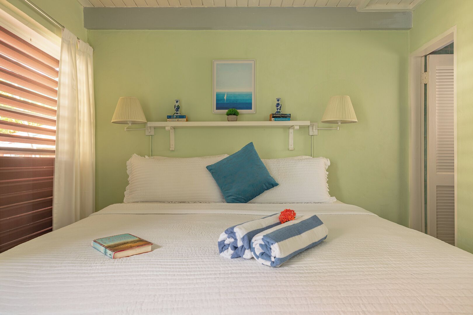 A neatly made bed with pillows, a book, and folded towels on a white bedspread.