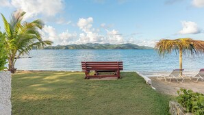 Un banco junto a un lago, con vistas a montañas, una palmera y un paraguas de paja.