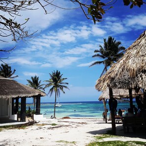 Eine Strandansicht mit strohgedeckten Hütten, Palmen und blauem Himmel.