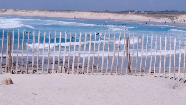 Une plage de sable avec une clôture en bois au premier plan et un ciel bleu clair en arrière-plan.