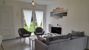 Un salon moderne avec un canapé gris, deux fauteuils, une table basse et un téléviseur à écran plat.