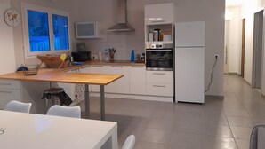 Une cuisine moderne avec des armoires blanches, un four encastré et un coin repas comprenant une table et des chaises en bois.