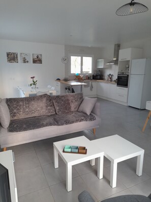 A modern living room with a grey sofa, a white coffee table, and a dining area with a white table and chairs.