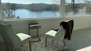 A room with two patterned chairs, a small table, and a view of a lake through large windows.