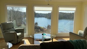 A living room with a view of a lake, a ceiling fan, and a glass coffee table.