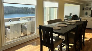 A dining area with a view of a lake, wooden flooring, and wicker furniture.