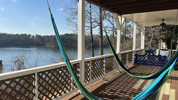 A wooden deck with a hammock, a blue bench, and a view of a lake.