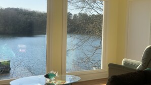 A room with a view of a lake, a glass table with Monopoly game boxes, and a chair.