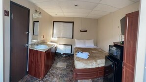 A hotel room with a bed, a desk, a TV, a bathroom with a sink and mirror, and a window with blinds.
